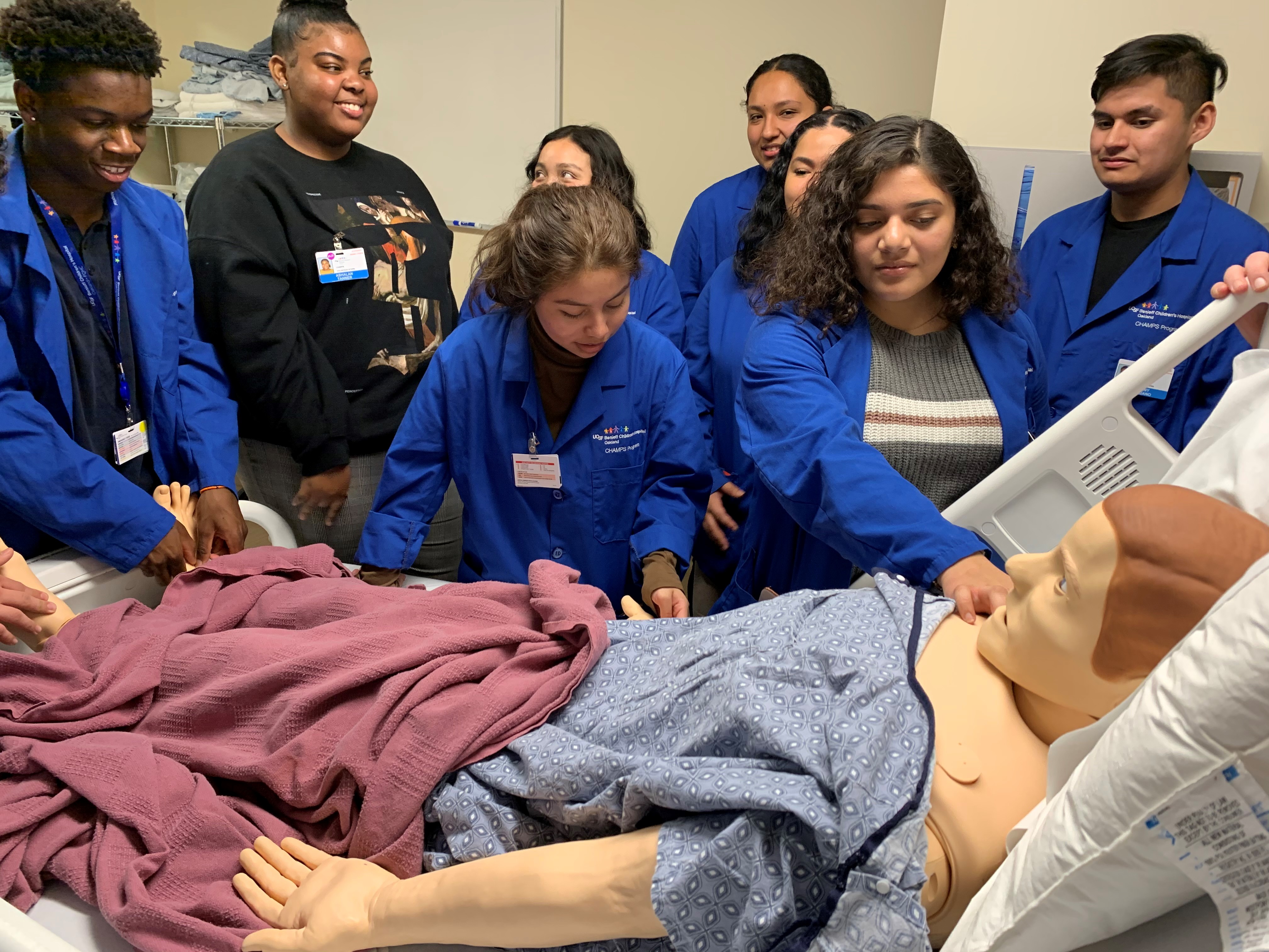 Group of 10 students leaning over the bed of a simulation patient doll.